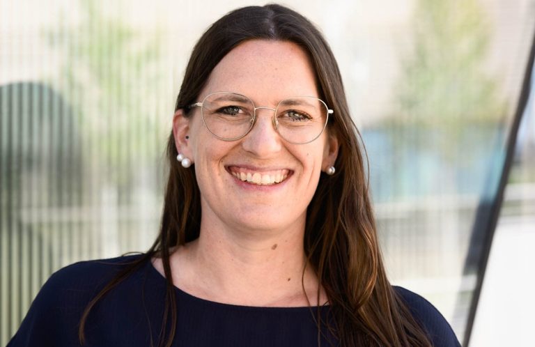 Lächelnde Frau mit lässiger Kleidung, Arme vor der Brust verschränkt.