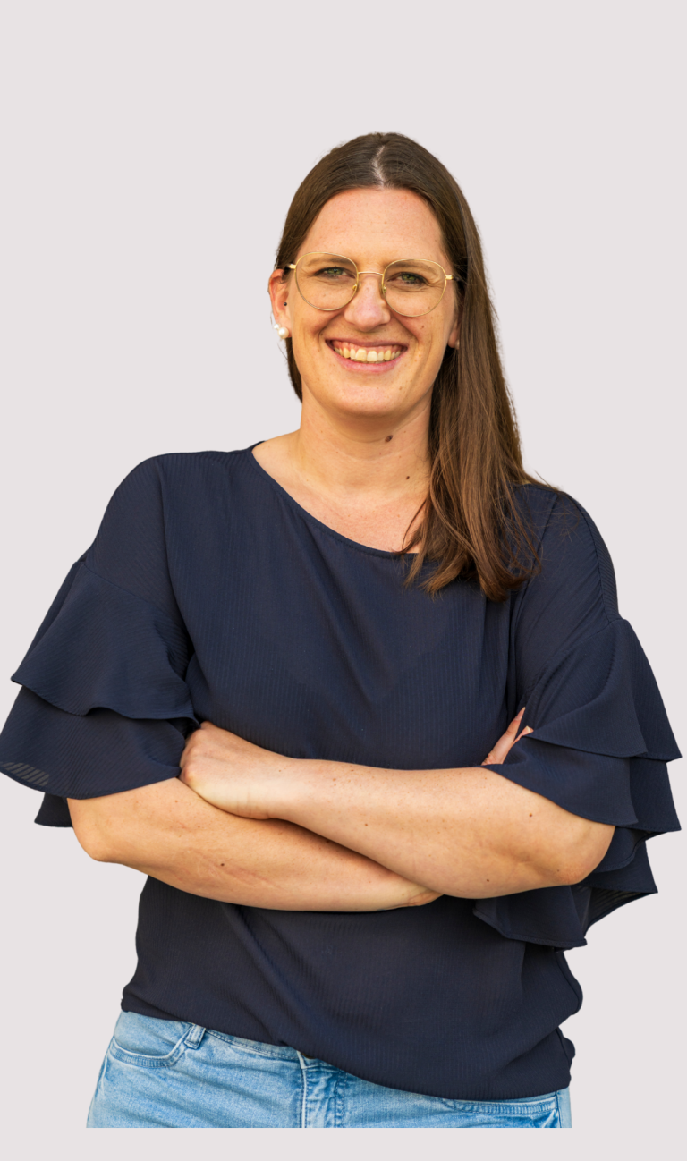 Kathrin Heimburger Lächelnde Frau mit langen Haaren in blauer Bluse und verschränkten Armen.