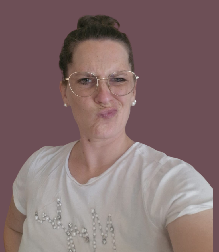 Kathrin Heimburger Junge Frau mit Brille, grauem Oberteil und Mappe, lächelt vor einer Wand.